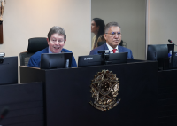 Homem branco sentado em uma bancada ao lado de homem pardo, ambos de terno escuro