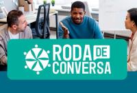 A imagem mostra um grupo de quatro pessoas sentadas em torno de uma mesa, em um ambiente de trabalho moderno e iluminado. Elas parecem estar envolvidas em uma conversa animada, trocando ideias e expressando opiniões com gestos e sorrisos. Ao fundo, há computadores e móveis de escritório, compondo um cenário colaborativo e profissional. A cena transmite um clima de diálogo, integração e troca de experiências, sugerindo um momento de reflexão coletiva, como uma roda de conversa.