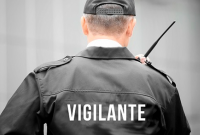 Homem de boné preto e jaleco preto de costa; o jaleco tem o nome Vigilante escrito em letras brancas ao centro