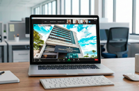 A imagem mostra um notebook aberto sobre uma mesa de trabalho, exibindo na tela a fachada de um prédio institucional durante uma videoconferência. Na tela, é possível ver a interface de uma reunião virtual, com participantes conectados no topo. O ambiente ao redor é um escritório moderno, com mesa de madeira, teclado, mouse, caderno e uma caneca. Ao fundo, aparecem cadeiras e mesas de trabalho, reforçando o contexto profissional e corporativo.