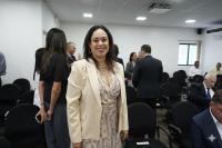 Mulher morena de cabelos pretos e roupa creme em pé e sorrindo para a foto
