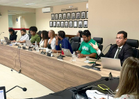 Várias pessoas, entre homens e mulheres, sentado em uma bancada participando de uma reunião