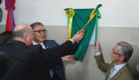 Foto de três homens de terno e gravata descerrando uma faixa verde e amarela