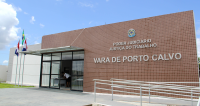 Fachada de prédio da Justiça do Trabalho em Porto Calvo, com parede revestida em pastilhas marrons e letreiro grande. À esquerda, entrada com portas de vidro e três bandeiras hasteadas. Há rampa de acessibilidade com corrimão na frente.