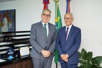 Dois homens idosos em pé posados para a foto. O da esquerda usa paletó cinza e o da direita, azul marinho. Ambos usam óculos