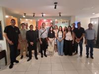 Um grupo de estudantes e profissionais posa para foto no interior do Memorial Pontes de Miranda. Os participantes estão organizados em fileira, em frente a painéis expositivos sobre a história jurídica. O ambiente é iluminado e apresenta elementos de museu, com informações históricas ao fundo. A maioria está com vestimenta social ou casual formal, sugerindo atividade acadêmica. A imagem registra um momento institucional durante visita guiada ao espaço.