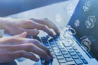 Mãos digitando em um notebook, em close. Sobre a imagem, há vários símbolos de cifrão ($) em destaque, sugerindo dinheiro ou finanças digitais. A cena tem tonalidade azulada e iluminação suave.