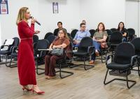 Mulher loira de vermelho falando em um frente a uma plateia