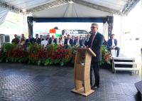 O desembargador-presidente do TRT-AL, Jasiel Ivo, discursa durante a abertura do I Arraial da Justiça e Cidadania. A solenidade ocorre em estrutura coberta, com autoridades e convidados posicionados no palco ao fundo. O espaço é ornamentado com arranjos de flores tropicais vermelhas e folhagens. Um painel de LED exibe a identidade visual do evento enquanto o magistrado fala ao púlpito.