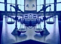 Foto de duas balanças da justiça em cima de uma mesa; ao fundo, janelas de vidros