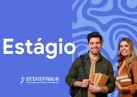 A imagem é uma peça gráfica institucional do Tribunal Regional do Trabalho da 19ª Região (AL) voltada à divulgação de estágio. Em destaque, a palavra “Estágio” aparece em letras brancas sobre fundo azul com elementos gráficos abstratos. À direita, dois jovens estudantes sorriem para a câmera enquanto seguram livros e materiais acadêmicos. Os estudantes usam mochilas e roupas casuais, transmitindo um clima de acolhimento e oportunidade profissional. 