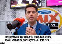 Homem de pele clara vestido de terno azul fala ao microfone veremelho e preto.