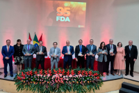 Várias pessoas em pé em frente a um palco com uma projeçaõ de luz escrito FDA