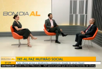 Há três pessoas sentadas. Sendo dois homens e uma mulher. Eles estão trajados de roupas escuras.Elas conversam. é um estúdio de filmagem. T