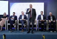 A imagem mostra autoridades e representantes de instituições durante a abertura da Semana do Trabalhador e da Trabalhadora, realizada no auditório da Santa Casa de Misericórdia de Maceió. Em destaque, um homem de terno faz uso da palavra ao microfone, enquanto os demais participantes acompanham a solenidade sentados no palco do evento.