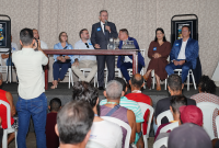 Vária pessoas sentada e um homem de de pé falando ao microfone