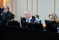 A imagem mostra três magistrados durante uma sessão de julgamento no plenário do Tribunal. Ao centro, um desembargador faz uso da palavra enquanto gesticula com a mão, demonstrando participação ativa nos debates. Os demais integrantes acompanham os trabalhos em seus respectivos postos, diante de monitores de computador, em ambiente formal e institucional.