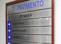 A imagem mostra uma placa de sinalização interna instalada em uma parede, indicando os setores localizados no 2º pavimento da 2ª Vara. No painel, aparecem direções para a Sala de Audiência, Gabinete dos Juízes e Banheiros, acompanhadas por setas indicativas. A placa possui fundo metálico, moldura em tom amadeirado e inscrições em azul e preto, características comuns de ambientes institucionais e administrativos.