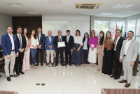 Grupo de pessoas posando para foto. Há homens e vestidos de terno. Um homem segura um papel.