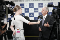 Uma repórter entrevista o desembargador Marcelo Vieira, ouvidor do TRT-AL, em frente a um painel institucional, enquanto câmeras registram a conversa.