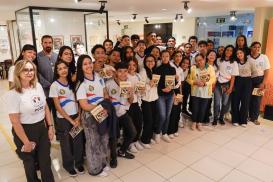Há um grupo de vários alunos com livros ma mão e dois adultos