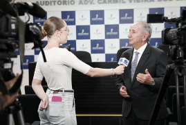 Uma repórter entrevista o desembargador Marcelo Vieira, ouvidor do TRT-AL, em frente a um painel institucional, enquanto câmeras registram a conversa.